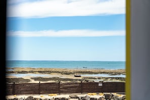 A coastal view with a wooden fence, rocky shore, and calm sea.
