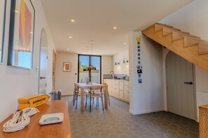 A modern kitchen with a wooden staircase, a dining area with a table and chairs, and a view through a glass door.