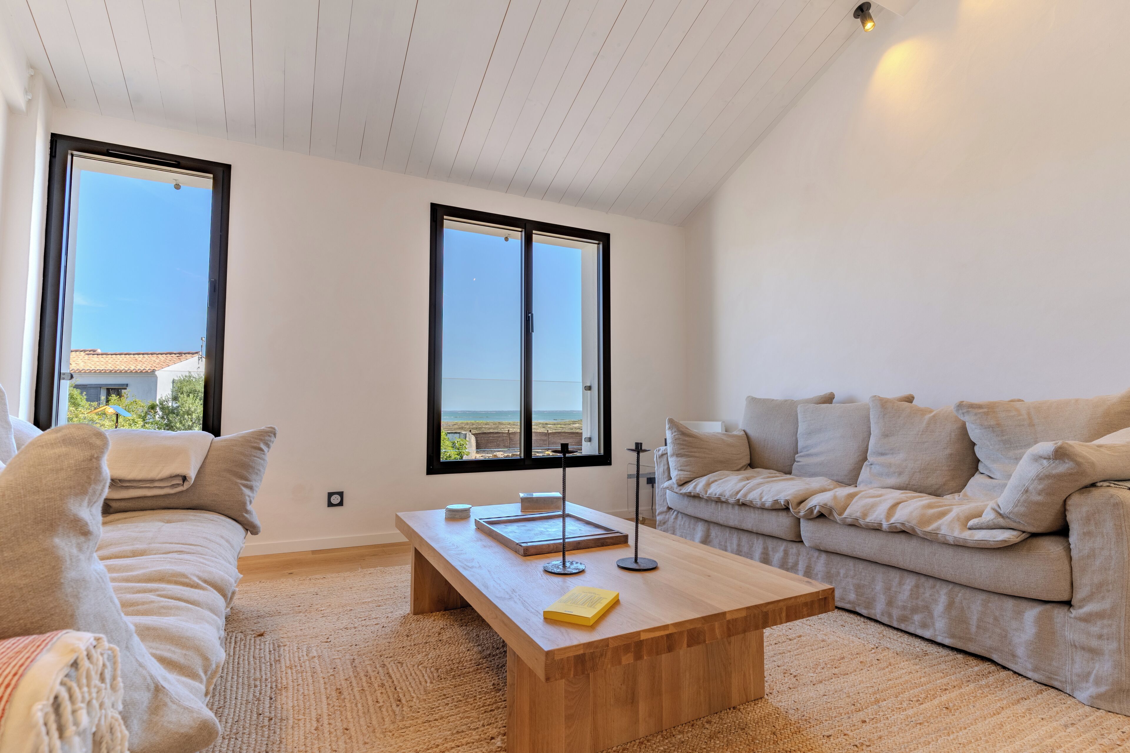 A spacious living room with a large window, a wooden coffee table, a beige sofa, and a second seating area.