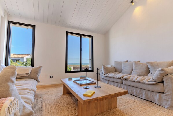 A spacious living room with a large window, a wooden coffee table, a beige sofa, and a second seating area.