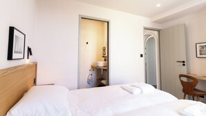 Habitación de hotel con una cama, un escritorio y un baño visible a través de una puerta abierta.