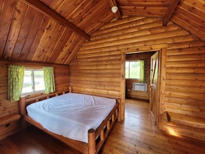 A wooden cabin with a bed, a window with curtains, and a door leading to another room.