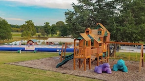 A playground with a wooden playhouse, a slide, and two animal-shaped swings. - Perryville RV Resort (Perryville)