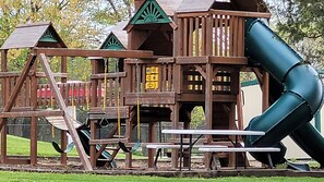 A playground with a slide, swings, and picnic tables.