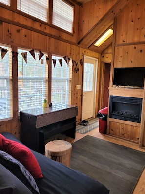 Interior acogedor de una cabaña con chimenea, televisor y cama con almohadas rojas.