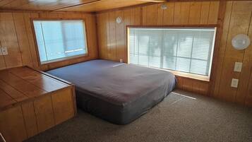 Een compacte kamer met een bed, een klein bureau en twee ramen met jaloezieën.