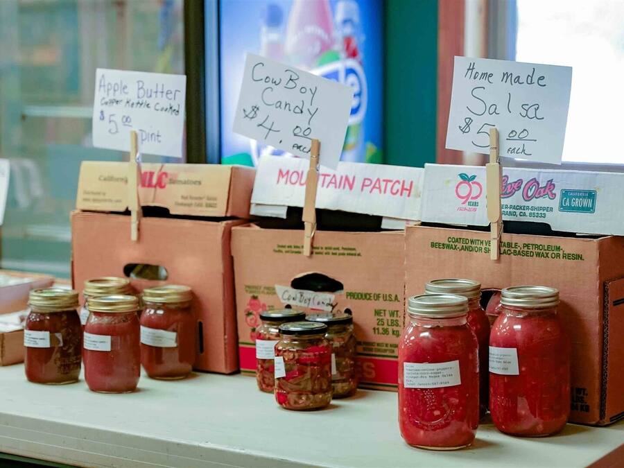 Exhibición de frascos con etiquetas que indican varios productos, como dulce de manzana y caramelo de vaquero, con precios de 5,00 y 4,00 dólares respectivamente.