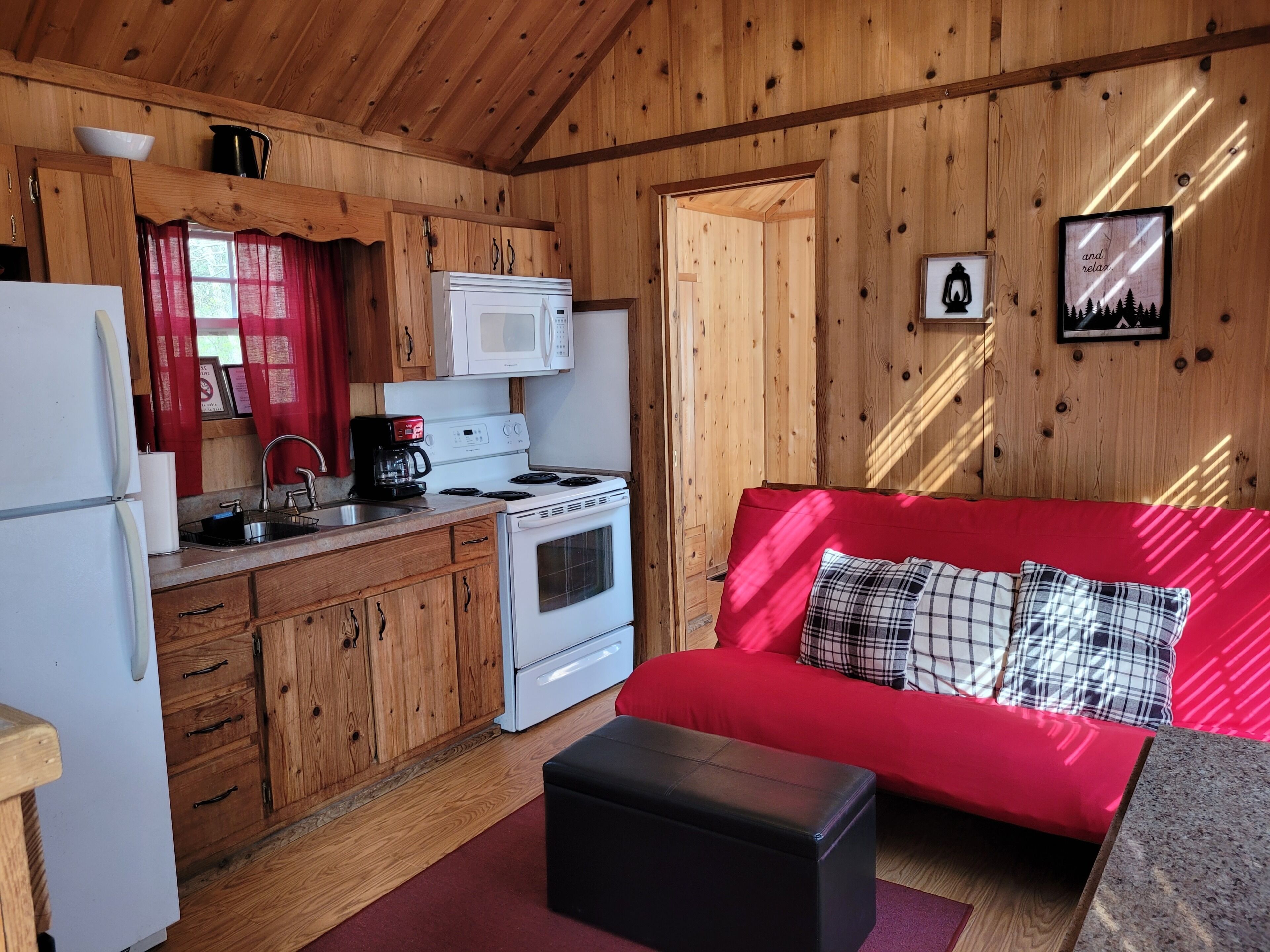 A compact kitchen with wooden cabinets, a white stove, and a red sofa with plaid cushions.