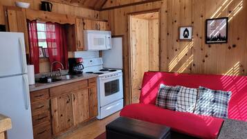 A compact kitchen with wooden cabinets, a white stove, and a red sofa with plaid cushions.