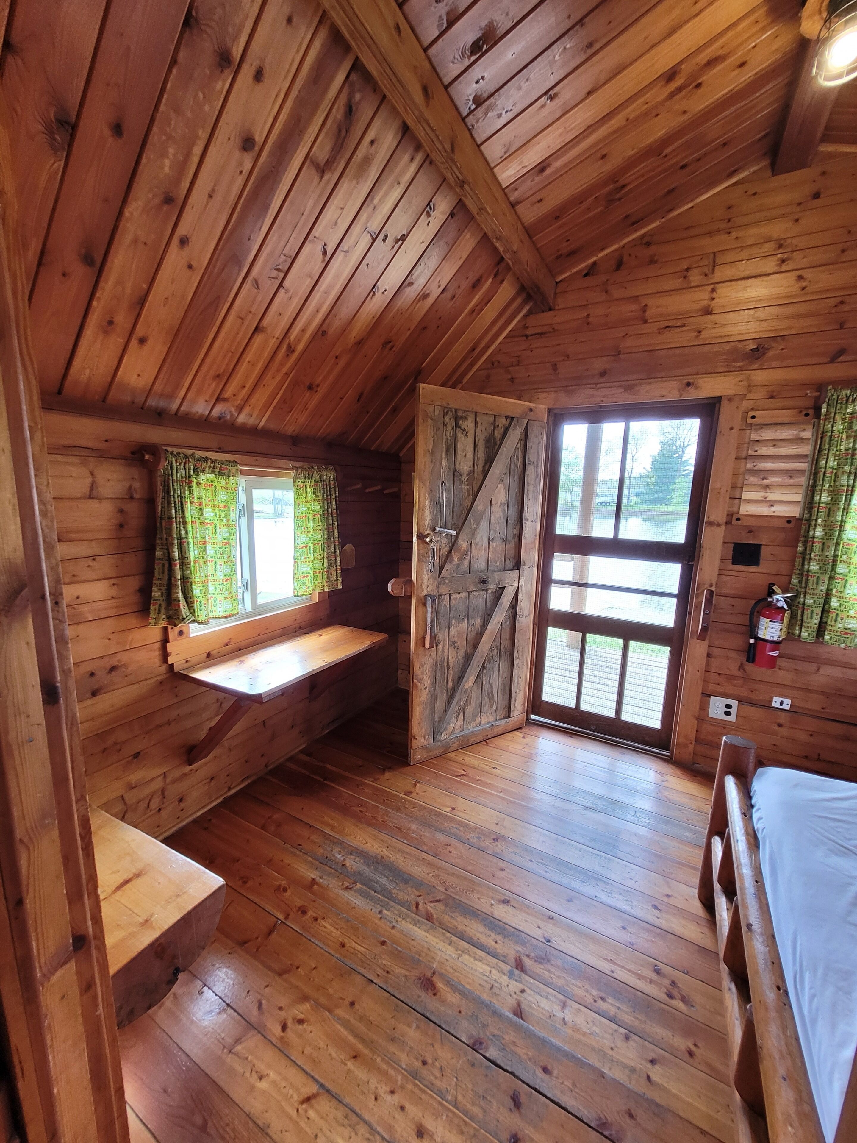 A wooden cabin with a loft bedroom, a bench, a bed, and a door leading outside.