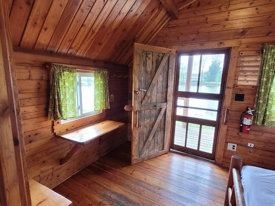 A wooden cabin with a loft bedroom, a bench, a bed, and a door leading outside.