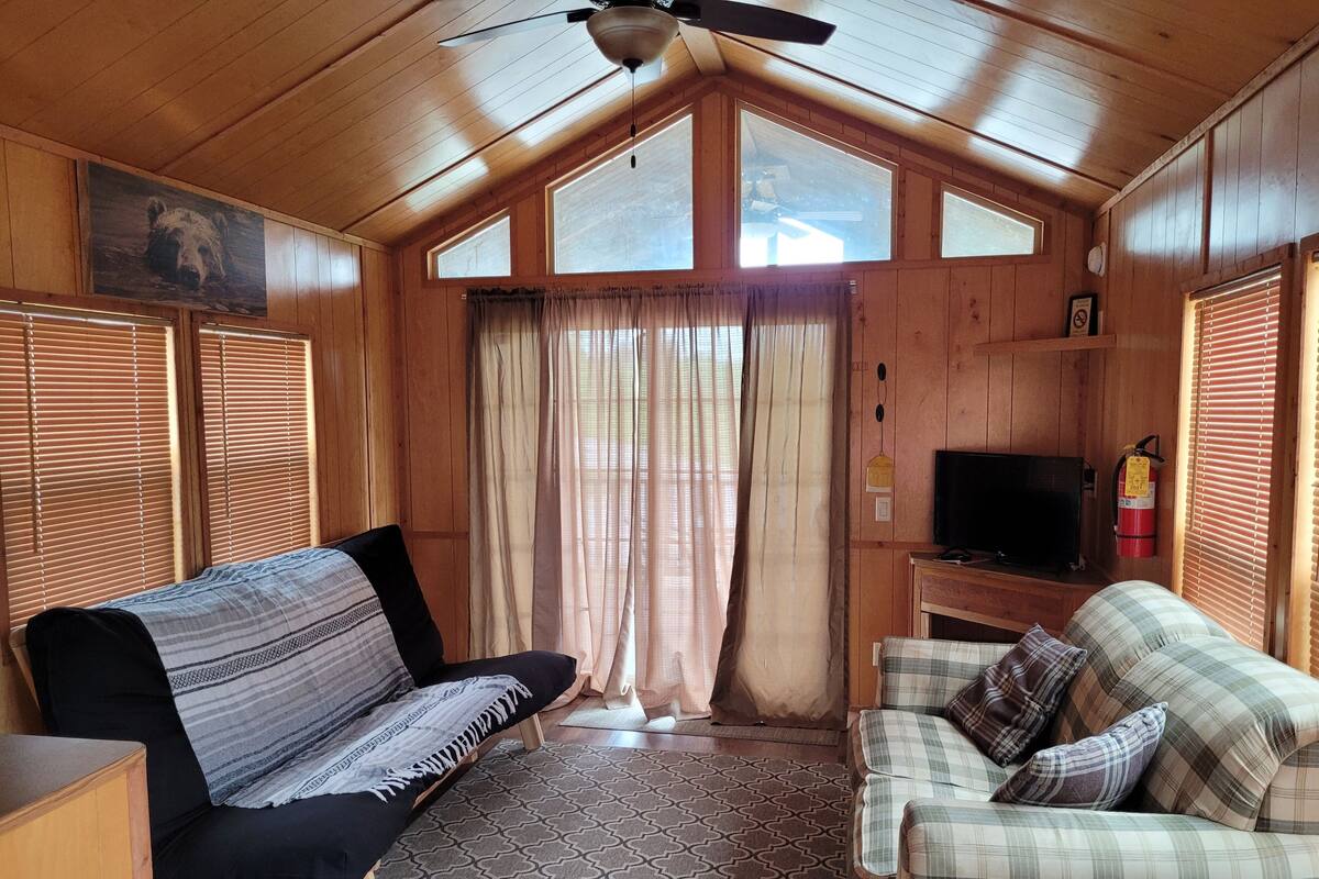 A cozy cabin interior with a sofa, a couch, a television, and a ceiling fan.