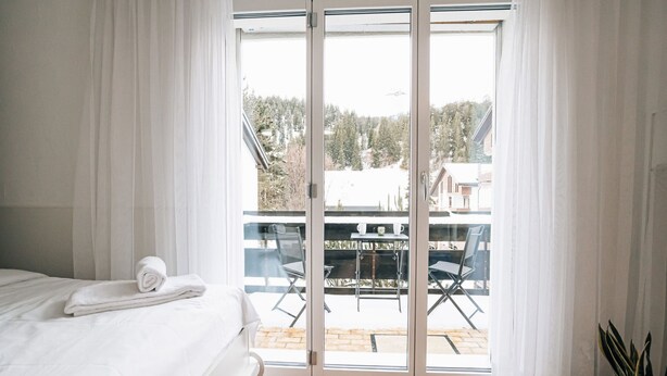 A bedroom with a bed, a balcony with a table and chairs, and a potted plant. - Laret 6-11 by Interhome (Laax)
