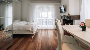 A modern hotel room with a bed, a desk, a chair, a television, and a fireplace. - Laret 6-11 by Interhome (Laax)