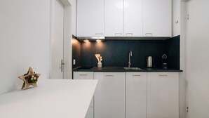 A modern kitchen with white cabinets, a black countertop, and a single white table. - Laret 6-11 by Interhome (Laax)