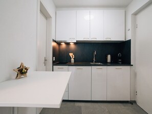 Eine moderne Küche mit weißen Schränken, einer schwarzen Arbeitsplatte und einem einzelnen weißen Tisch.