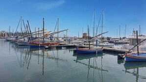 Ein Yachthafen mit mehreren vor Anker liegenden Booten, ruhigem Wasser und Gebäuden im Hintergrund.
