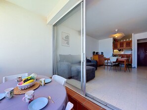 A dining area with a table set for two, a sofa, and a kitchen in the background. - Port Saint Ange by Interhome (Le Barcarès)