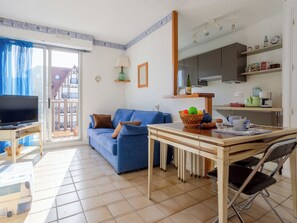Ein Wohnzimmer mit Sofa, Fernseher, Esstisch mit Stühlen, Küchenzeile mit Schränken und einem Balkon mit Blick.