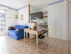A compact living space with a blue sofa, a dining table with a chair, a kitchen area, and a large window. - Horizon Marin by Interhome (Cabourg)