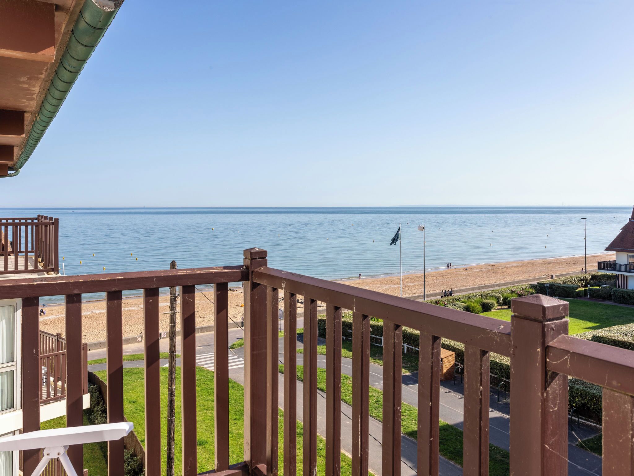 A balcony with a view of the sea, a wooden deck, and a grassy area with a pathway.