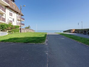A paved pathway leading to a body of water, flanked by a building with balconies and a small wooden structure. - Horizon Marin by Interhome (Cabourg)