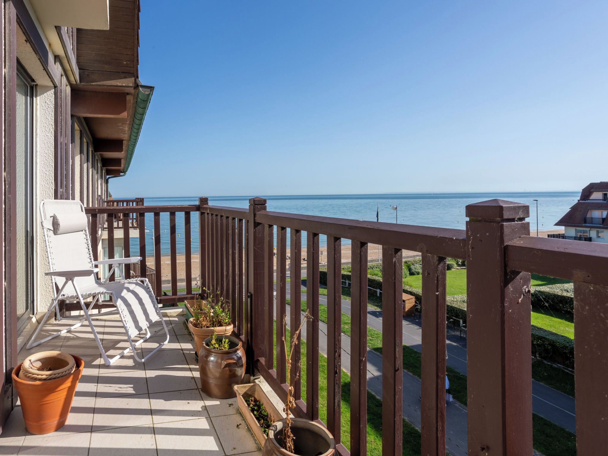 A balcony with a white chair, potted plants, and a view of the sea.