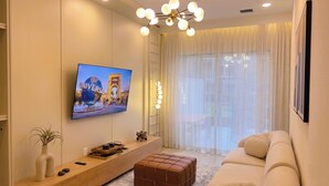 A living room with a TV mounted on the wall, a sofa, a coffee table, and a decorative floor lamp. - Luxury 5BR/5BA - Villa at Paradiso Grande Near Universal, Sea World and more (Orlando)