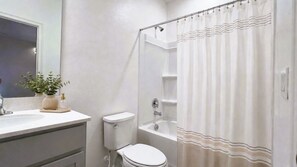 Un baño con inodoro, lavamanos, bañera y cortina de ducha.