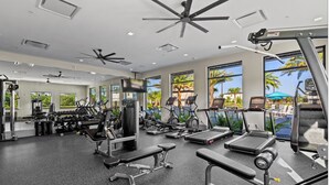 A gym with various exercise equipment, large windows, and a ceiling fan. - Luxury 5BR/5BA - Villa at Paradiso Grande Near Universal, Sea World and more (Orlando)