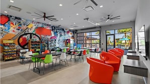 A modern indoor space with ceiling fans, tables, chairs, and a colorful mural. - Luxury 5BR/5BA - Villa at Paradiso Grande Near Universal, Sea World and more (Orlando)