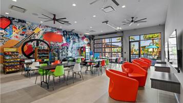 A modern indoor space with ceiling fans, tables, chairs, and a colorful mural.