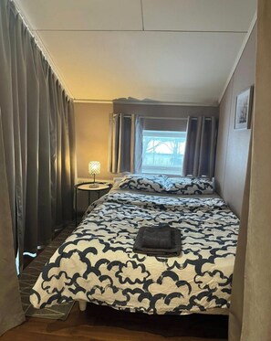 A bedroom with a bed, a bedside table, a window with curtains, and a view of the outside.