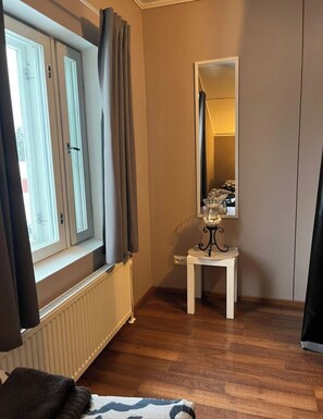 Ett rum med ett fönster, ett element, ett litet bord med en dekorativ prydnad och en spegel på väggen.
