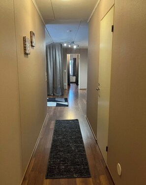 Un pasillo con pisos de madera, un tapete negro y una puerta a la derecha.