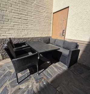 Un patio con una mesa y sillas de mimbre, un sofá gris y una puerta de madera.