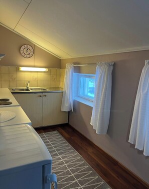 Ett kompakt kök med en klocka, ett fönster med gardiner och en mönstrad matta.