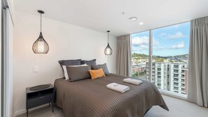 Una habitación de hotel moderna con una cama grande, dos lámparas colgantes, una mesita de noche y vistas a la ciudad.