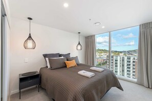 A modern hotel room with a large bed, two pendant lights, a nightstand, and a view of the city. - 2BR Skyline Views - Cozy HydeLane Stay w Amenities (Wellington)
