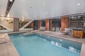 An indoor swimming pool with a clear view of the pool, a staircase, and a seating area with a hot tub. - 2BR Skyline Views - Cozy HydeLane Stay w Amenities (Wellington)
