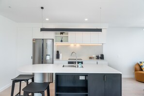 A modern kitchen with a central island, stainless steel appliances, and a minimalist design. - 2BR Skyline Views - Cozy HydeLane Stay w Amenities (Wellington)