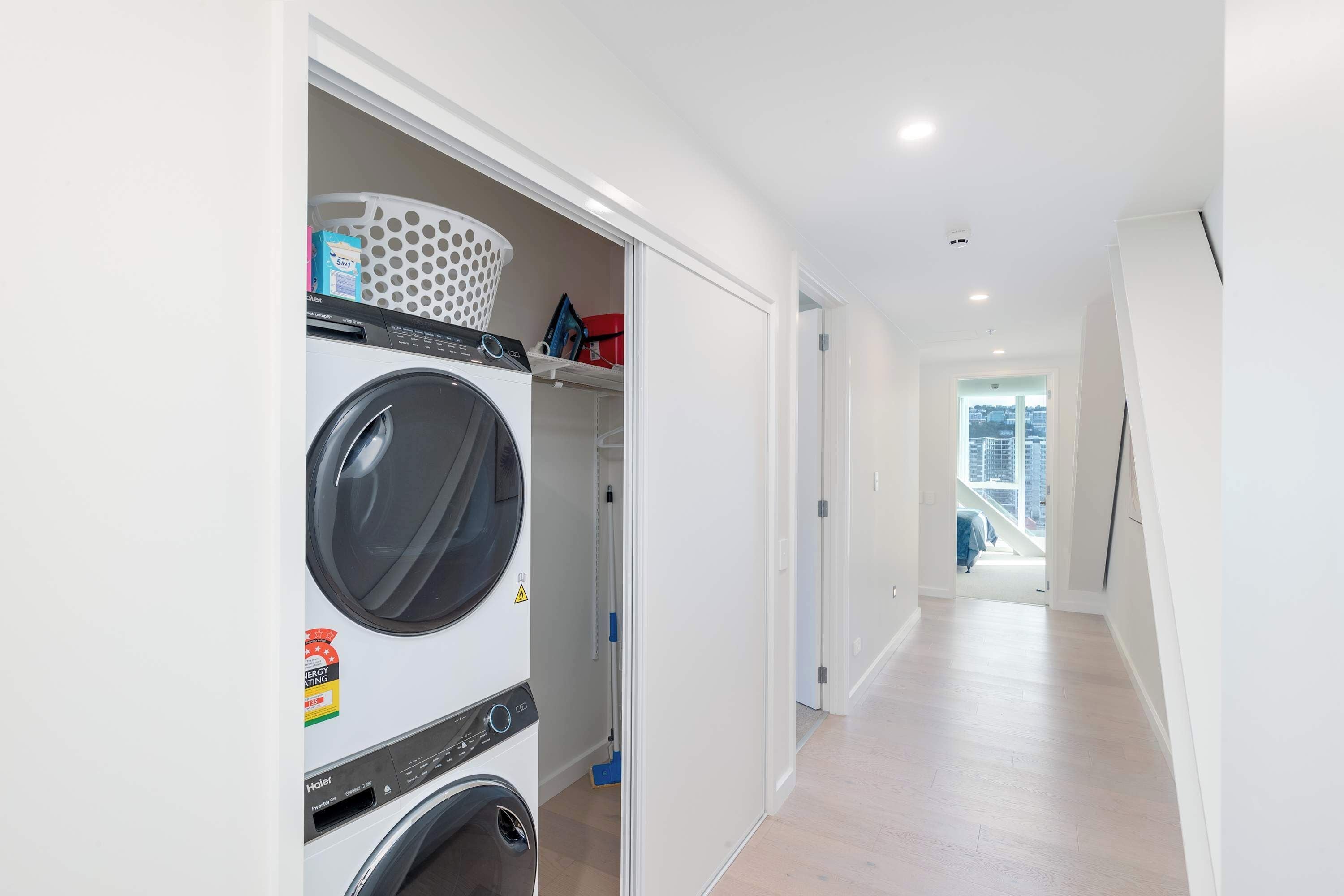 A laundry room with a front-loading washer and dryer, a laundry basket, and a mop.