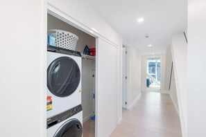 Ein Waschraum mit einer Frontlader-Waschmaschine und einem Trockner, einem Wäschekorb und einem Mop.