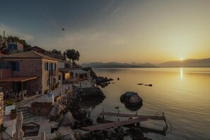 A coastal property with a stone building, outdoor seating, and a dock extending into calm waters. - Deluxe Studio - Sea Mansion Lefkada (Lefkada)
