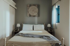 A bed with white bedding, two bedside tables with lamps, a wall-mounted artwork, and a window with curtains. - Deluxe Studio - Sea Mansion Lefkada (Lefkada)