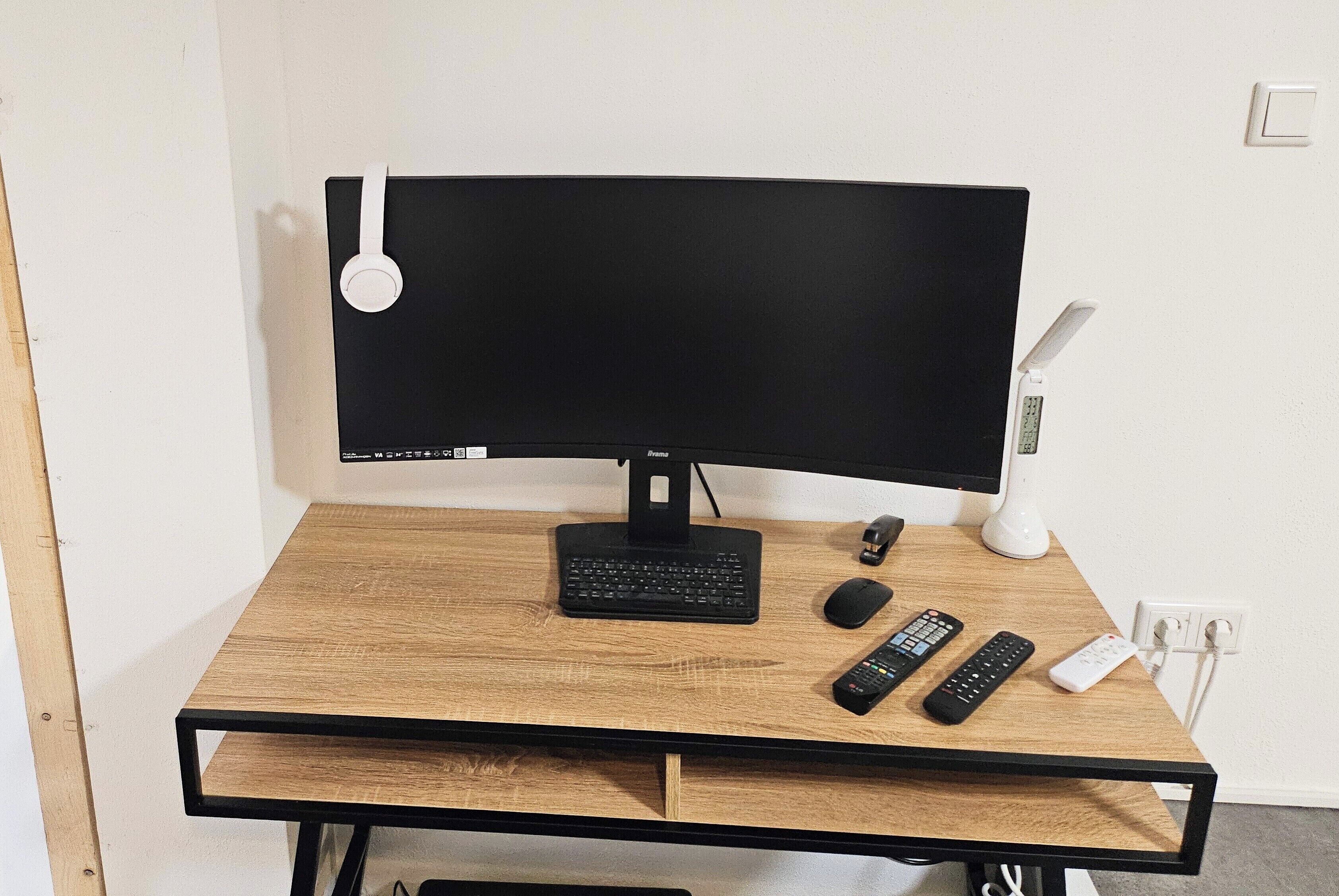 Et træbord med en sort skærm, tastatur, mus og to fjernbetjeninger.