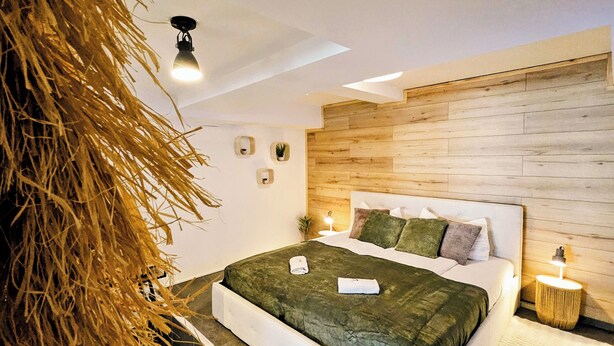 Quarto moderno com cabeceira de madeira, colcha verde e uma pequena mesa de cabeceira com abajur.