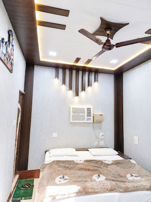 A bedroom with a bed, a ceiling fan, recessed lighting, an air conditioning unit, and a patterned bedspread. - Hotel Shree Inn Uttarakhand (Sitarganj)