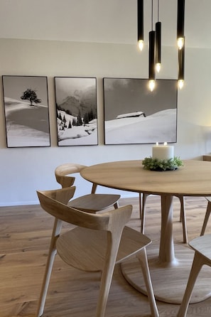Uma sala de jantar com uma mesa de madeira redonda, quatro cadeiras e três fotografias emolduradas de paisagens de inverno na parede.