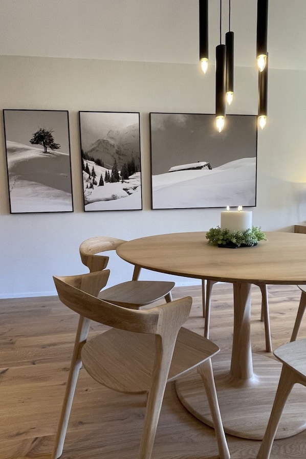 Ein Essbereich mit einem runden Holztisch, vier Stühlen und drei gerahmten Winterlandschaftsfotografien an der Wand.